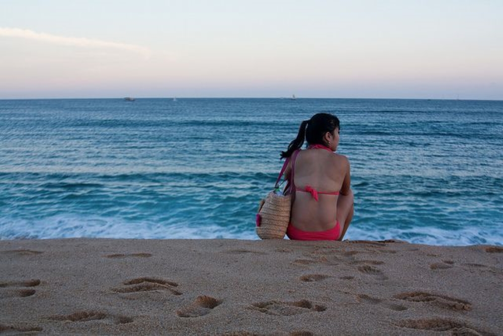kobieta na plaży w czerwonym stroju kąpielowym i torbą