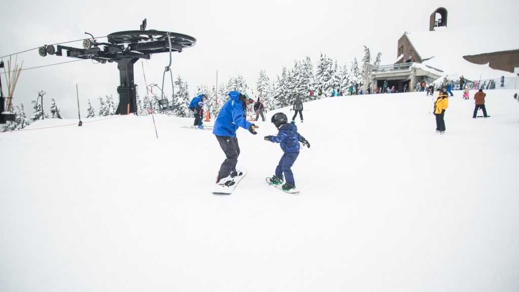 mężczyzna w niebieskiej kurtce zimowej i dziecko na snowboardzie